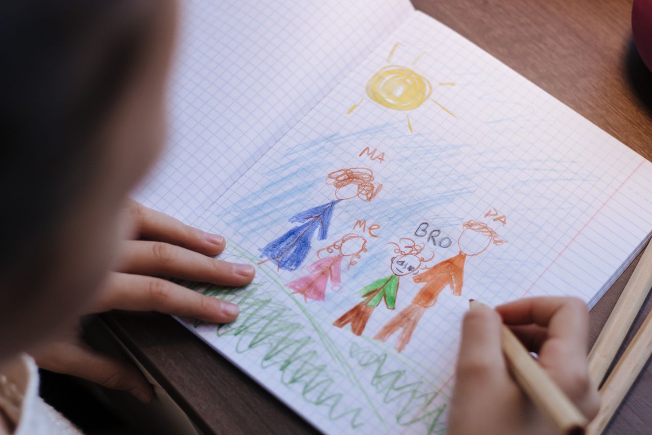 Young child drawing with crayons at a table, practicing fine motor skills