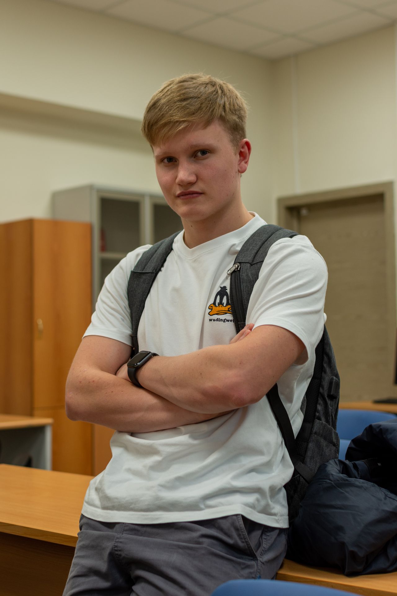 Young child wearing a backpack walking toward a classroom door alongside a supportive adult