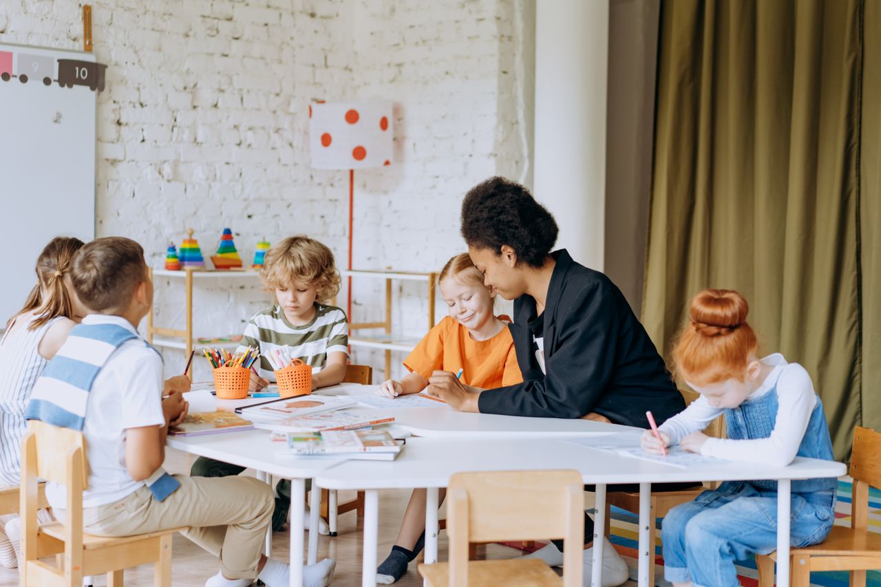 Adult working with a small group of young children at a table with books and pencils