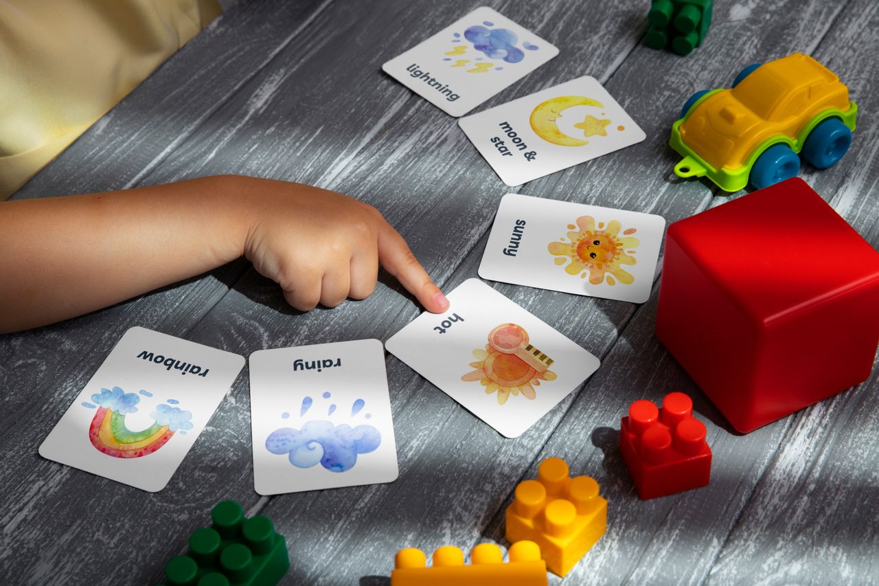A child points at a colorful picture card on a table, an example of visual communication support