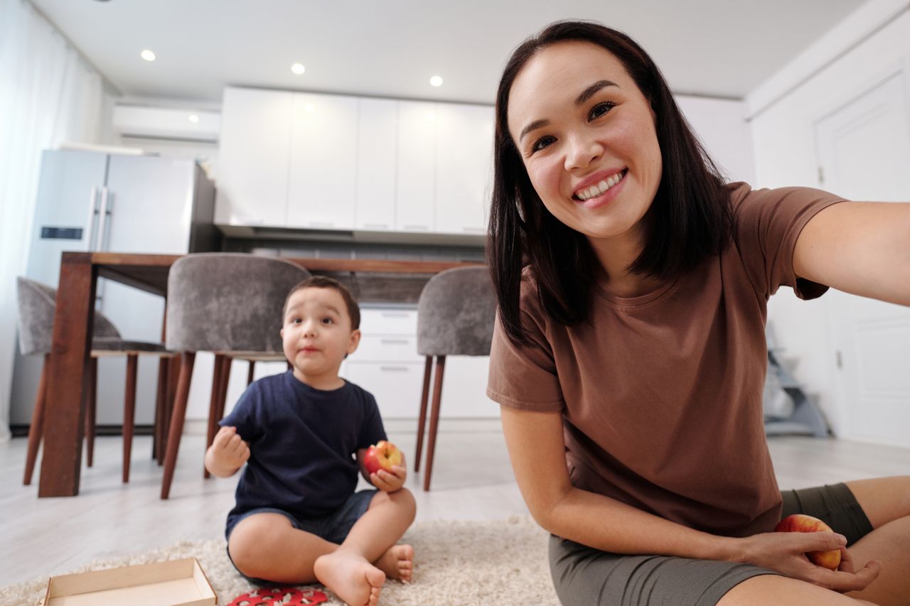 A mother and her young child sitting together on the floor indoors, sharing a moment of family time